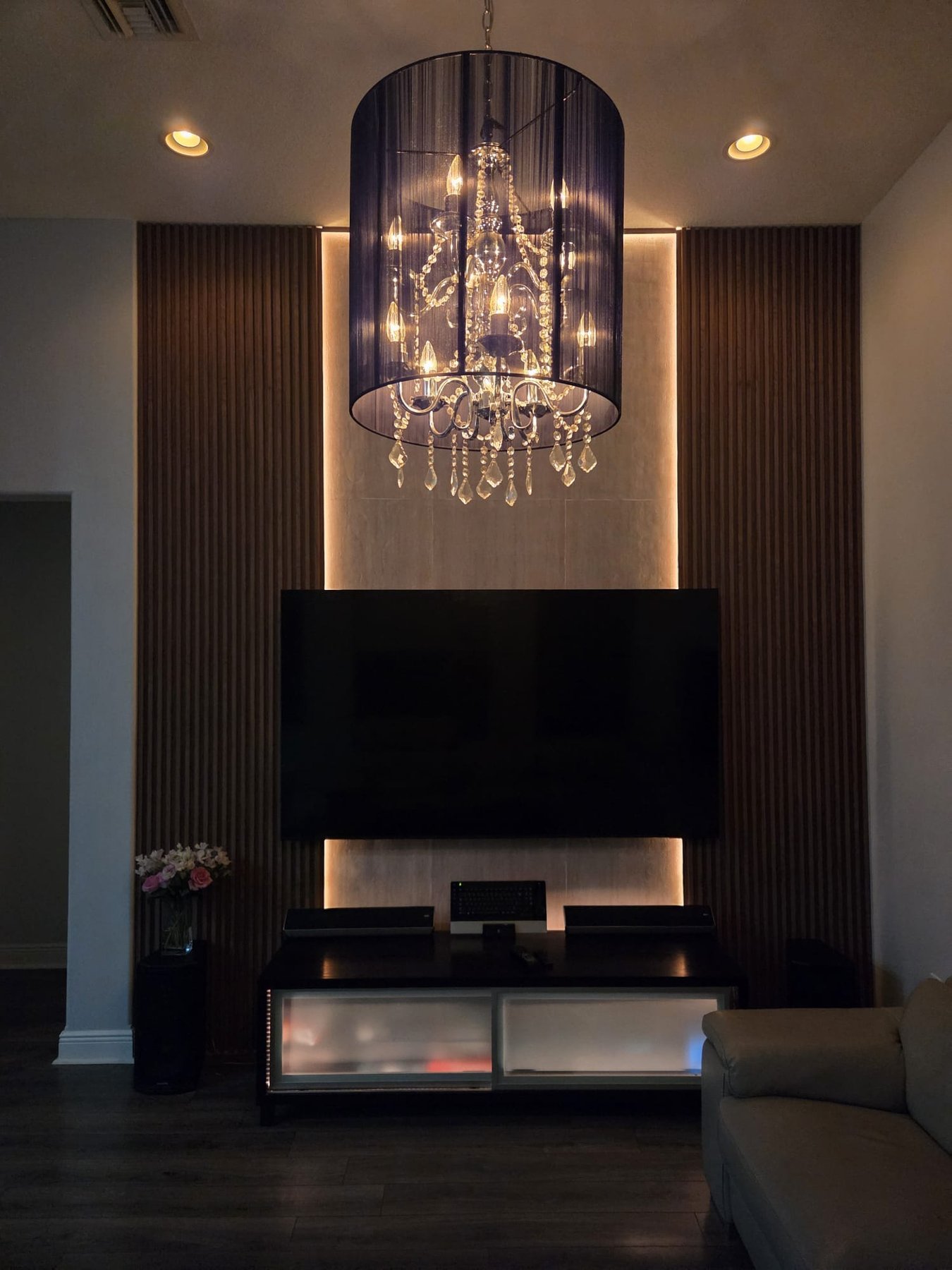 Completed wood-slat television feature wall with warm LED lighting and illuminated chandelier